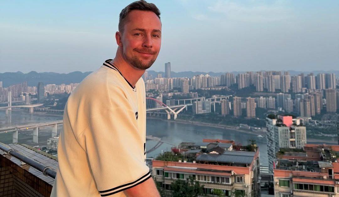 CadiaN стоит в белой футболке на фоне города